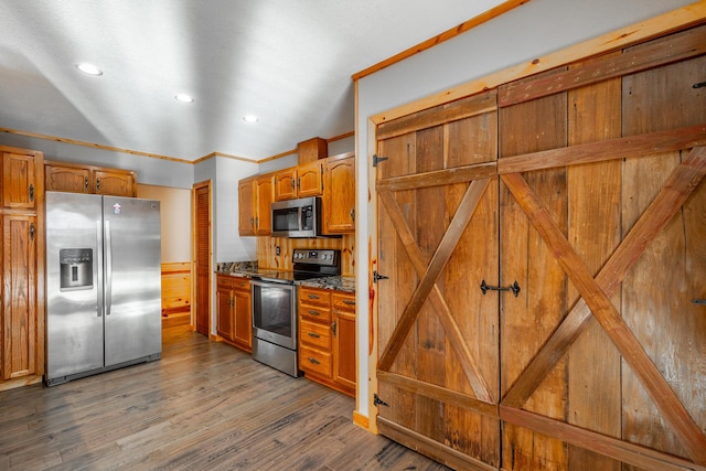 kitchen with appliances with stainless steel finishes, dark hardwood / wood-style flooring, crown molding, and dark stone countertops