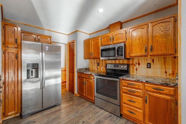 kitchen with dark hardwood / wood-style floors, wooden walls, stainless steel appliances, and ornamental molding