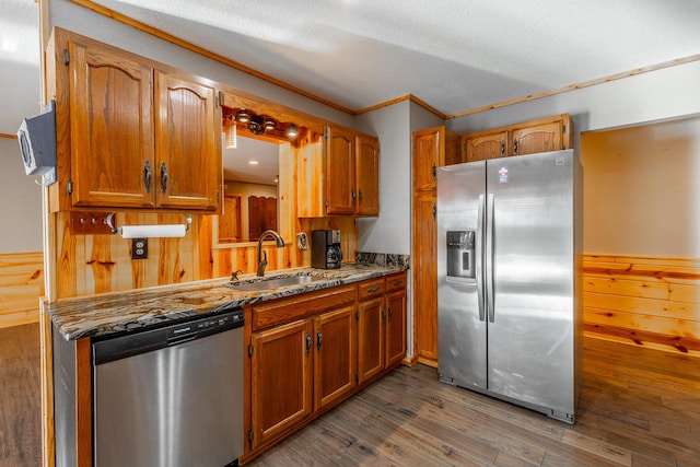 kitchen with a textured ceiling, appliances with stainless steel finishes, dark wood-type flooring, wooden walls, and sink