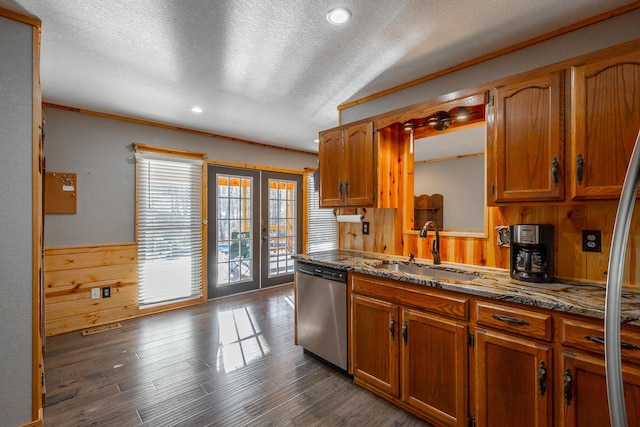 kitchen with a textured ceiling, dishwasher, french doors, sink, and wood walls