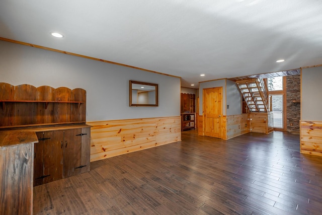 unfurnished living room with dark wood-type flooring, crown molding, and wooden walls