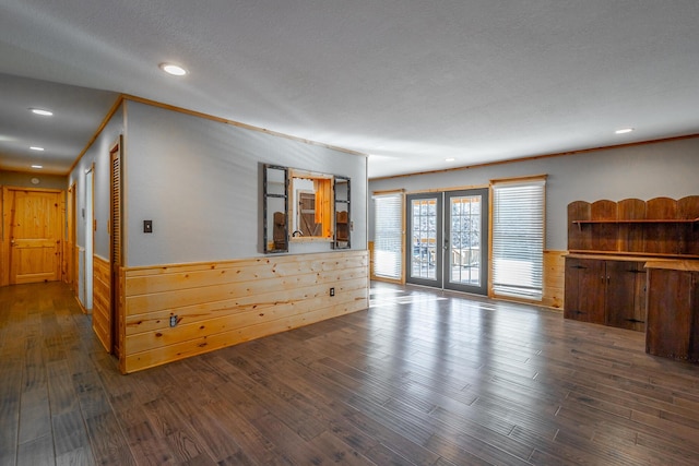 unfurnished living room with dark wood-type flooring, crown molding, french doors, and wooden walls