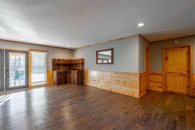 unfurnished living room with a textured ceiling, dark wood-type flooring, crown molding, and wood walls