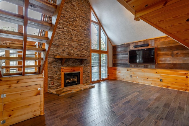 unfurnished living room with wood-type flooring, wooden walls, a fireplace, high vaulted ceiling, and beam ceiling