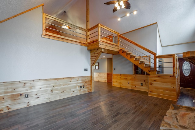 unfurnished living room featuring wooden walls, ceiling fan, dark wood-type flooring, high vaulted ceiling, and ornamental molding