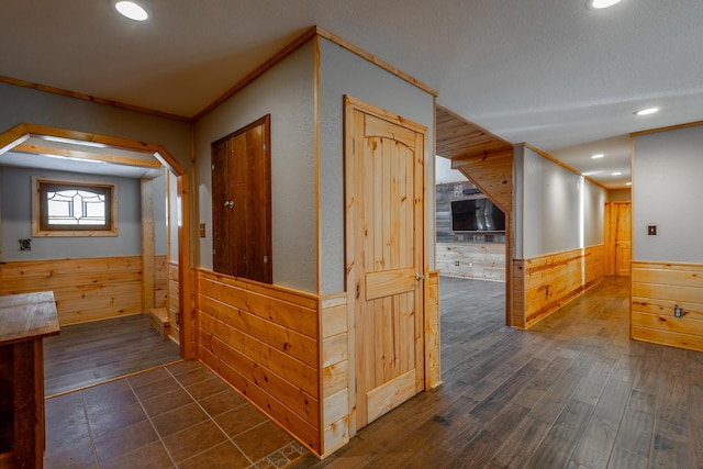 hall with crown molding, dark hardwood / wood-style flooring, and wooden walls