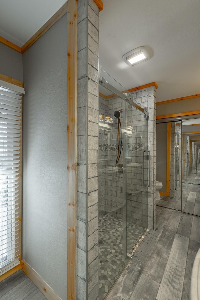 bathroom featuring toilet, ornamental molding, hardwood / wood-style floors, and a shower with door