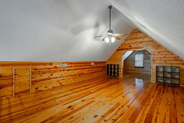 bonus room featuring a textured ceiling, lofted ceiling, wood-type flooring, wooden walls, and ceiling fan