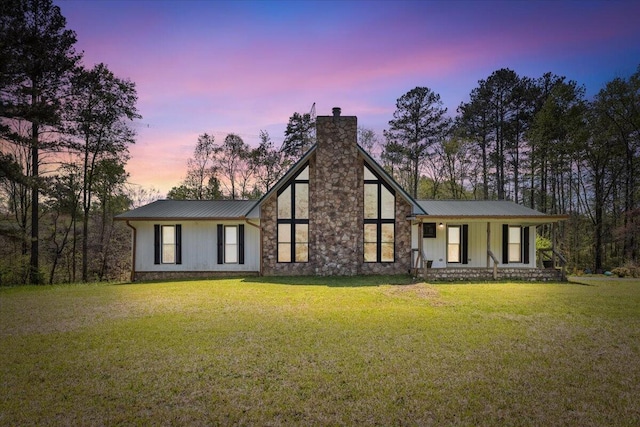 back of house at dusk featuring metal roof, a chimney, and a lawn