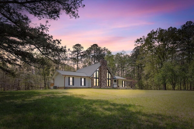 view of front of home featuring a front yard, central AC unit, metal roof, and a chimney