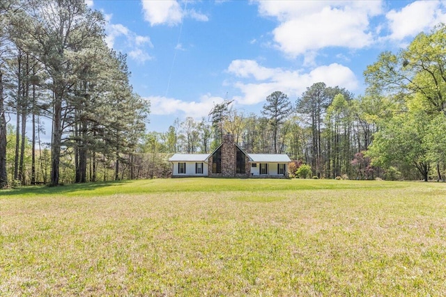 view of front facade featuring a wooded view, a chimney, and a front lawn