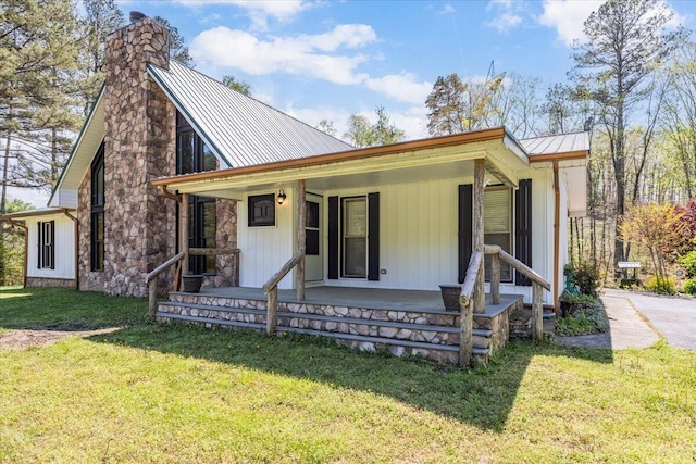 view of front of home with a chimney, a front lawn, a porch, a standing seam roof, and metal roof
