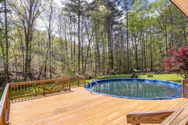 view of pool featuring a yard, a deck, a forest view, and a covered pool