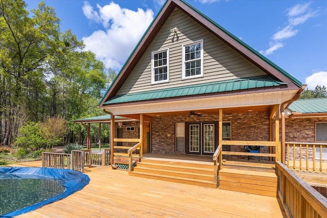 back of house with french doors, metal roof, stone siding, and a wooden deck
