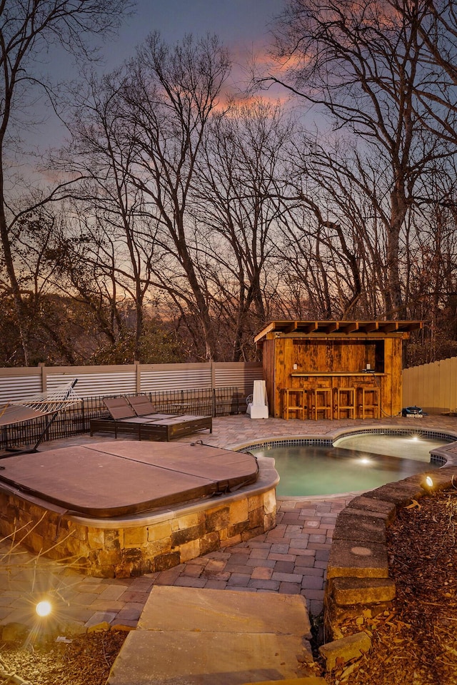 pool at dusk featuring a bar and a patio