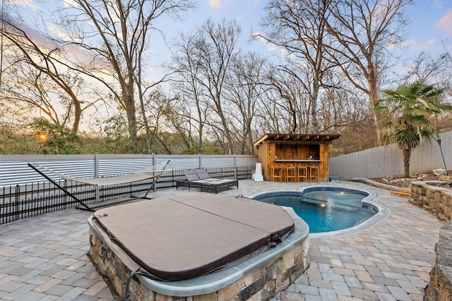 pool at dusk with exterior bar, a covered hot tub, and a patio area