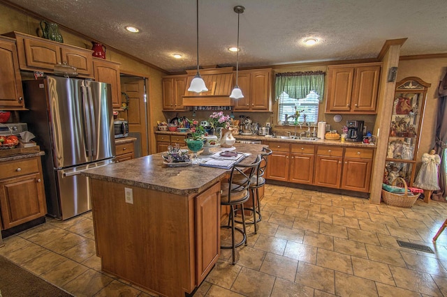 kitchen with sink, pendant lighting, a textured ceiling, a kitchen island, and appliances with stainless steel finishes