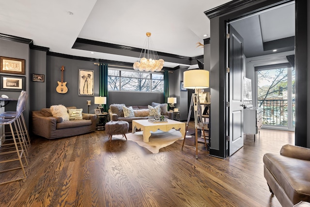 living room with a tray ceiling, crown molding, a chandelier, and dark hardwood / wood-style floors