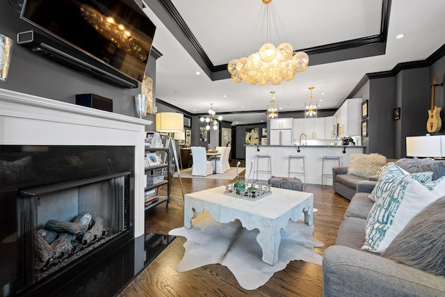 living room featuring a notable chandelier, a raised ceiling, crown molding, and dark wood-type flooring