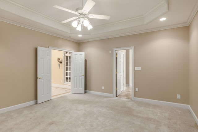 empty room with light colored carpet, ceiling fan, a raised ceiling, and ornamental molding