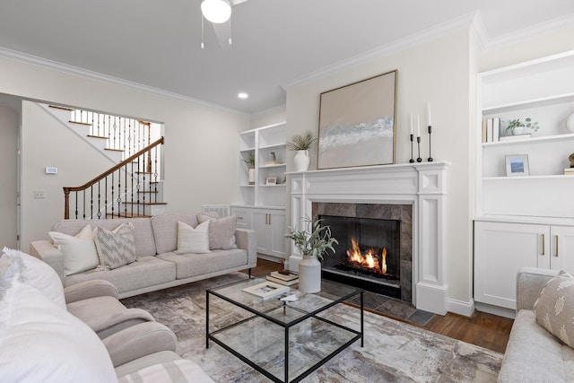 living room with ornamental molding, dark wood-type flooring, ceiling fan, a fireplace, and built in shelves