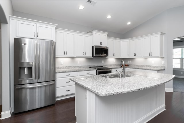 kitchen with appliances with stainless steel finishes, white cabinets, vaulted ceiling, and a center island with sink