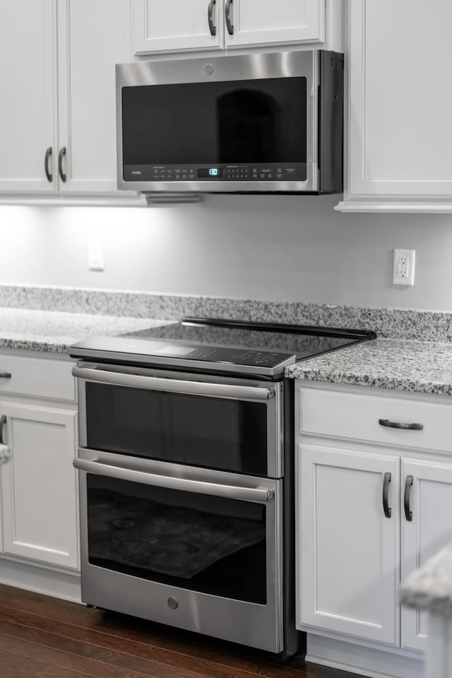 kitchen with stainless steel appliances, white cabinetry, and light stone counters