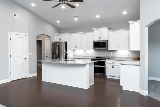 kitchen featuring light stone counters, stainless steel appliances, a center island with sink, white cabinetry, and ceiling fan