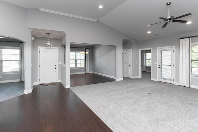 unfurnished living room featuring lofted ceiling, dark wood-type flooring, ornamental molding, and ceiling fan with notable chandelier