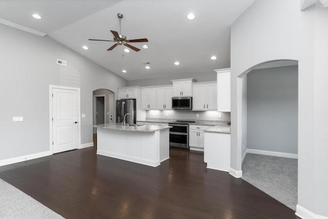 kitchen with light stone countertops, a center island with sink, white cabinets, appliances with stainless steel finishes, and ceiling fan