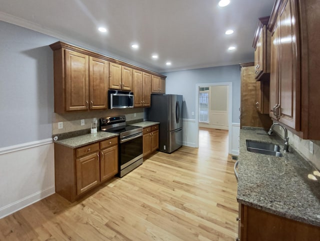 kitchen with ornamental molding, stainless steel appliances, sink, dark stone countertops, and light hardwood / wood-style floors