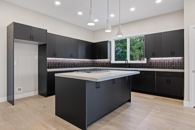 kitchen with sink, decorative light fixtures, a center island, light hardwood / wood-style flooring, and backsplash