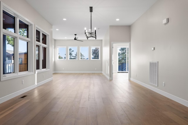 unfurnished dining area with ceiling fan with notable chandelier and wood-type flooring