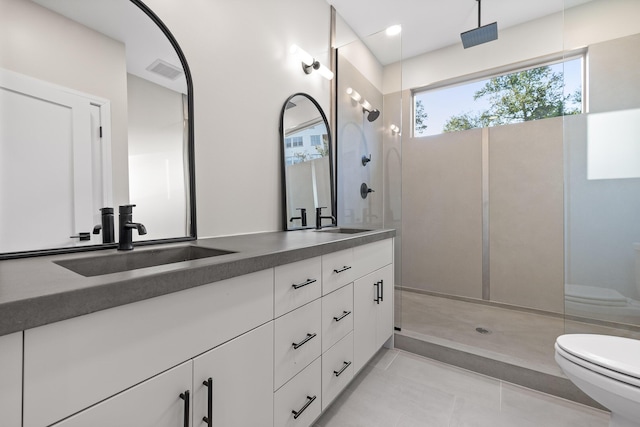 bathroom with a tile shower, toilet, tile patterned flooring, and vanity