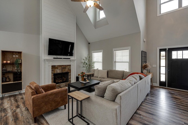 living room featuring a high ceiling, dark hardwood / wood-style flooring, ceiling fan, and a stone fireplace