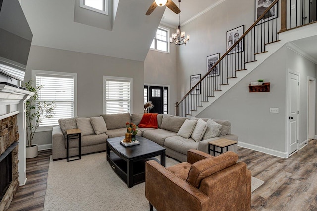 living room featuring hardwood / wood-style floors, a towering ceiling, ceiling fan with notable chandelier, a fireplace, and ornamental molding