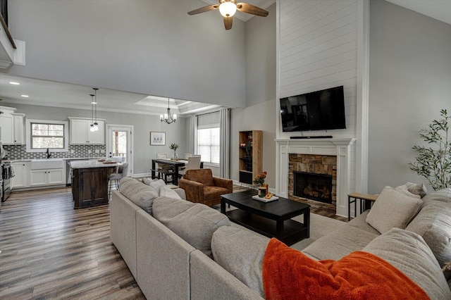 living room featuring a stone fireplace, lofted ceiling, ceiling fan with notable chandelier, and wood-type flooring