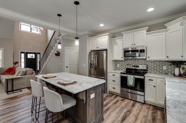 kitchen featuring appliances with stainless steel finishes, pendant lighting, white cabinetry, and light stone counters