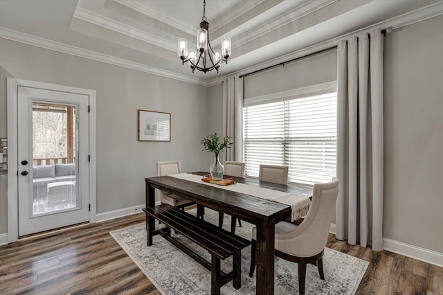 dining area with ornamental molding, an inviting chandelier, a tray ceiling, and dark hardwood / wood-style flooring