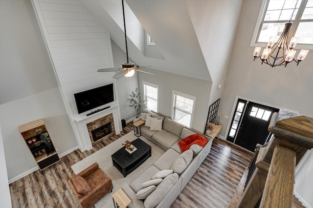 living room featuring wood-type flooring, a towering ceiling, ceiling fan with notable chandelier, and a fireplace