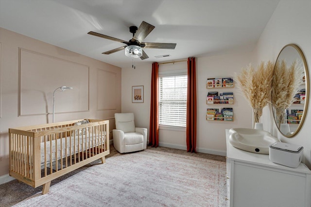 bedroom featuring a crib, light carpet, and ceiling fan