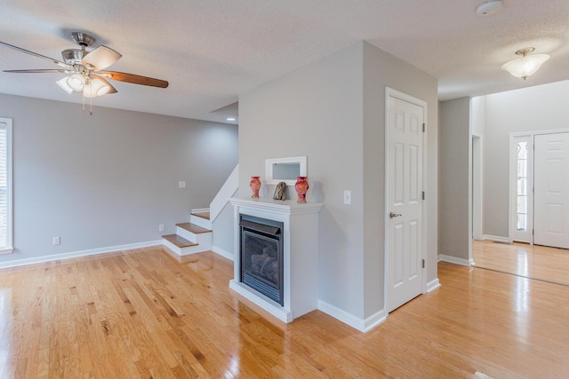 unfurnished living room with a textured ceiling, ceiling fan, and light wood-type flooring