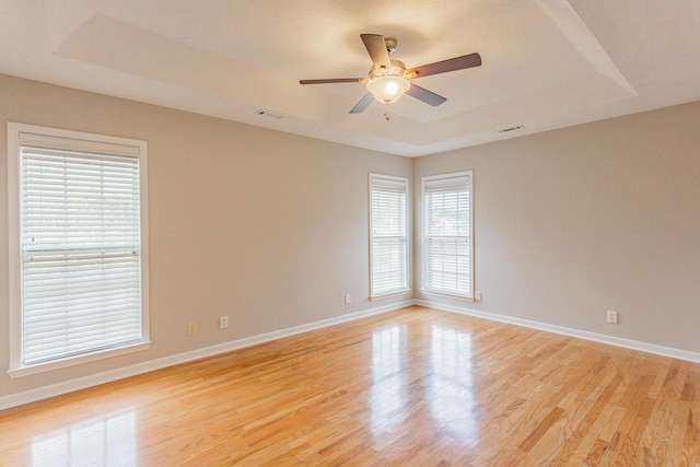 unfurnished room featuring a raised ceiling, ceiling fan, and light hardwood / wood-style floors