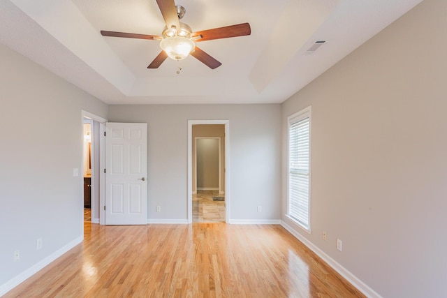 unfurnished bedroom featuring ceiling fan, light hardwood / wood-style floors, and a tray ceiling