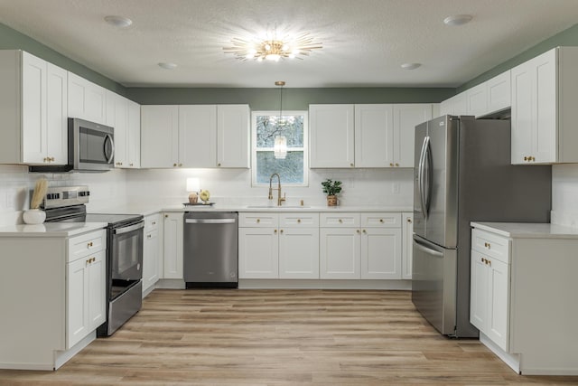 kitchen with sink, stainless steel appliances, white cabinetry, and hanging light fixtures