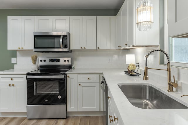 kitchen with decorative backsplash, light wood-type flooring, white cabinets, appliances with stainless steel finishes, and sink