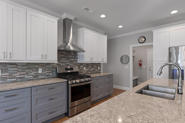 kitchen featuring sink, white cabinetry, appliances with stainless steel finishes, wall chimney range hood, and backsplash