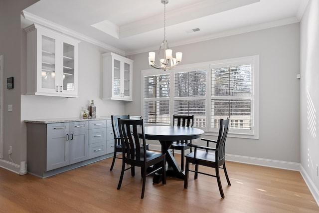 dining area featuring crown molding, a tray ceiling, a chandelier, and light hardwood / wood-style flooring