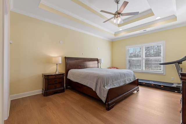 bedroom featuring crown molding, light hardwood / wood-style flooring, ceiling fan, and a tray ceiling