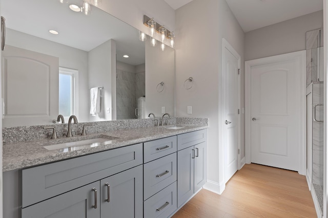 bathroom featuring double vanity, a stall shower, wood finished floors, and a sink